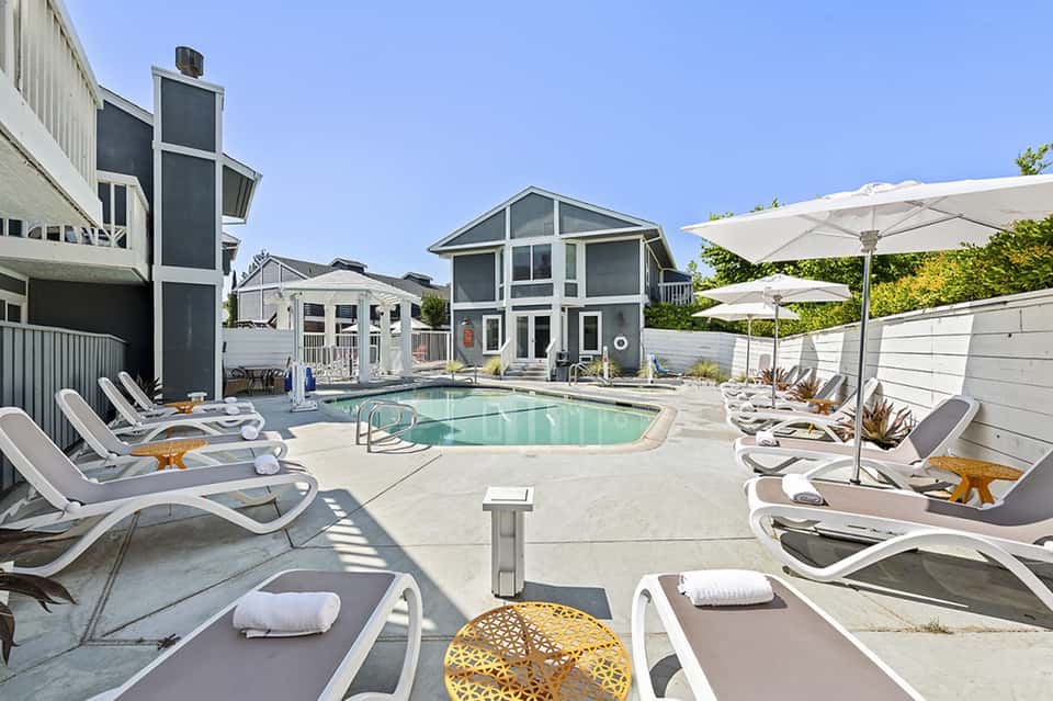 Residential pool area with modern homes, lounge chairs, umbrellas, and landscaping