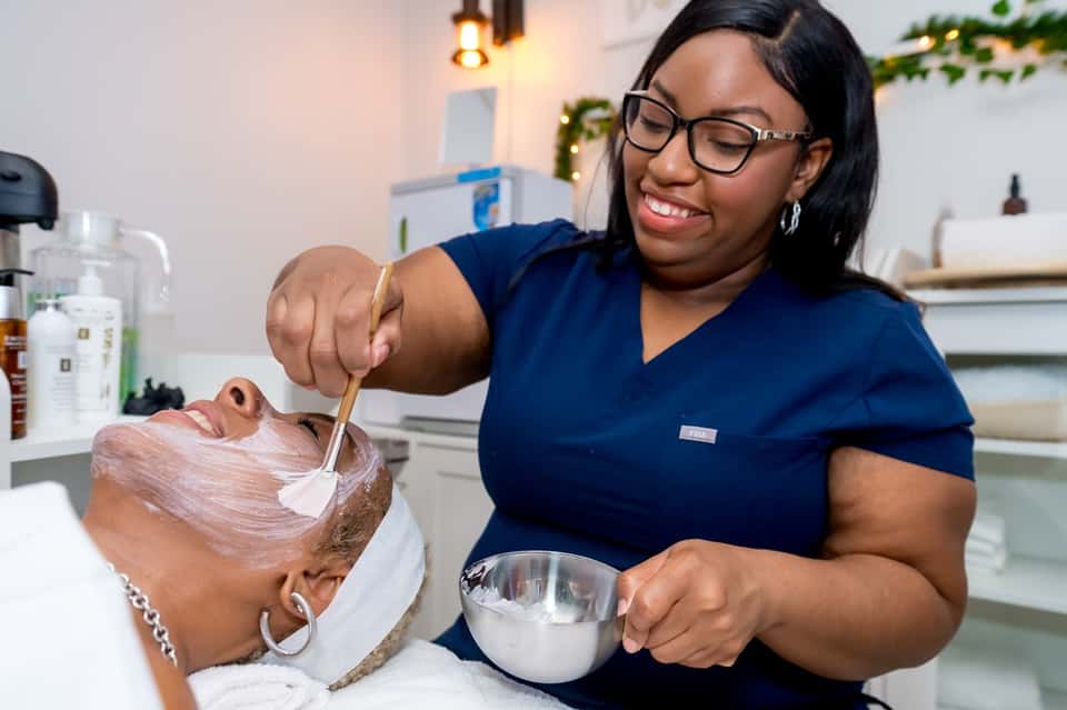 Spa professional applying hair treatment mask to client's hair in modern wellness salon