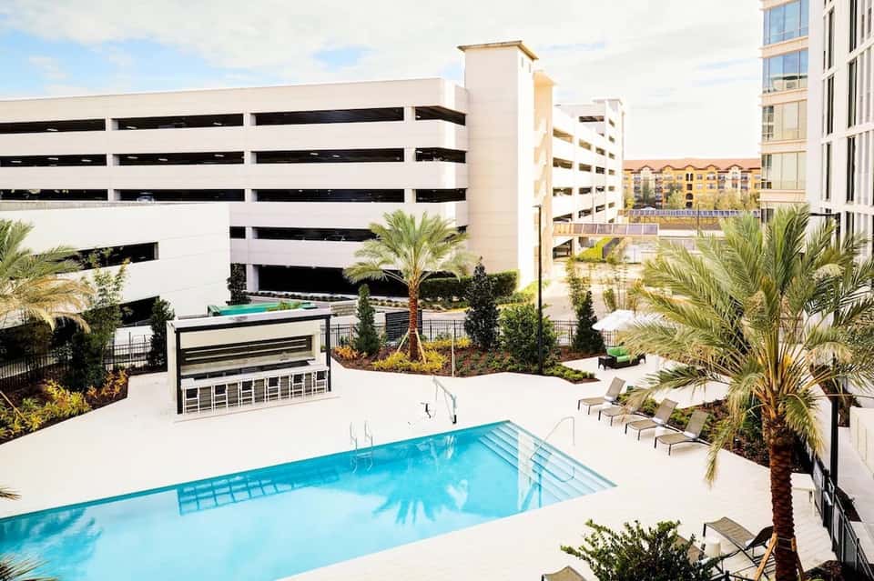 Contemporary urban hotel courtyard pool with parking structure, palm trees, and loungers