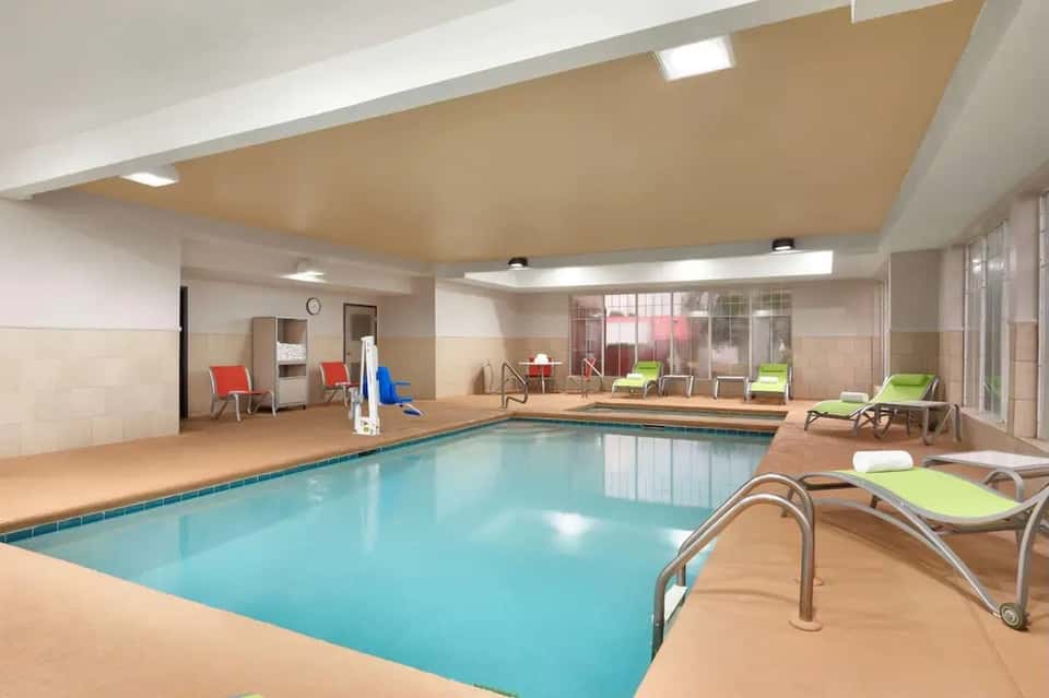 Indoor heated swimming pool with green loungers and observation windows