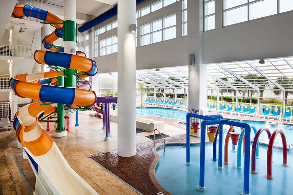 Indoor water park with colorful spiral water slide, shallow pools, and large windows