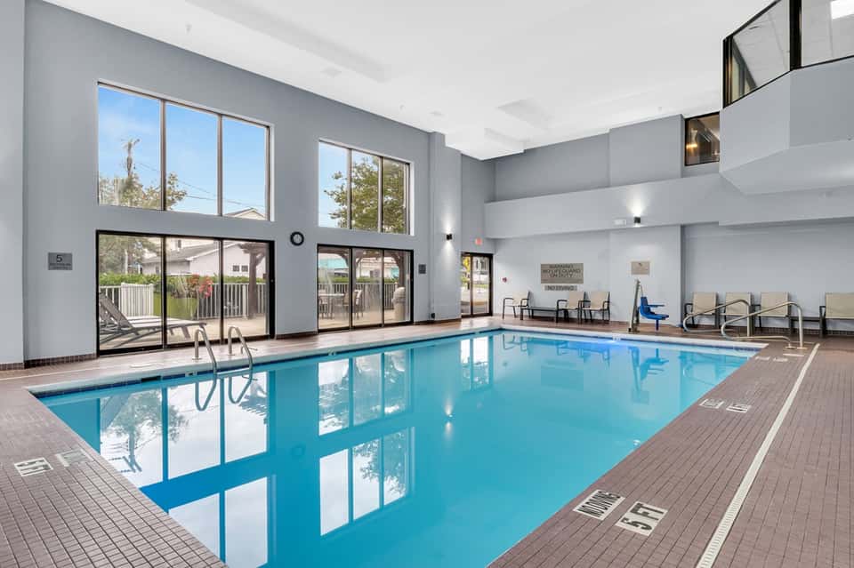 Large indoor swimming pool with crystal clear water, floor-to-ceiling windows, and lounge seating