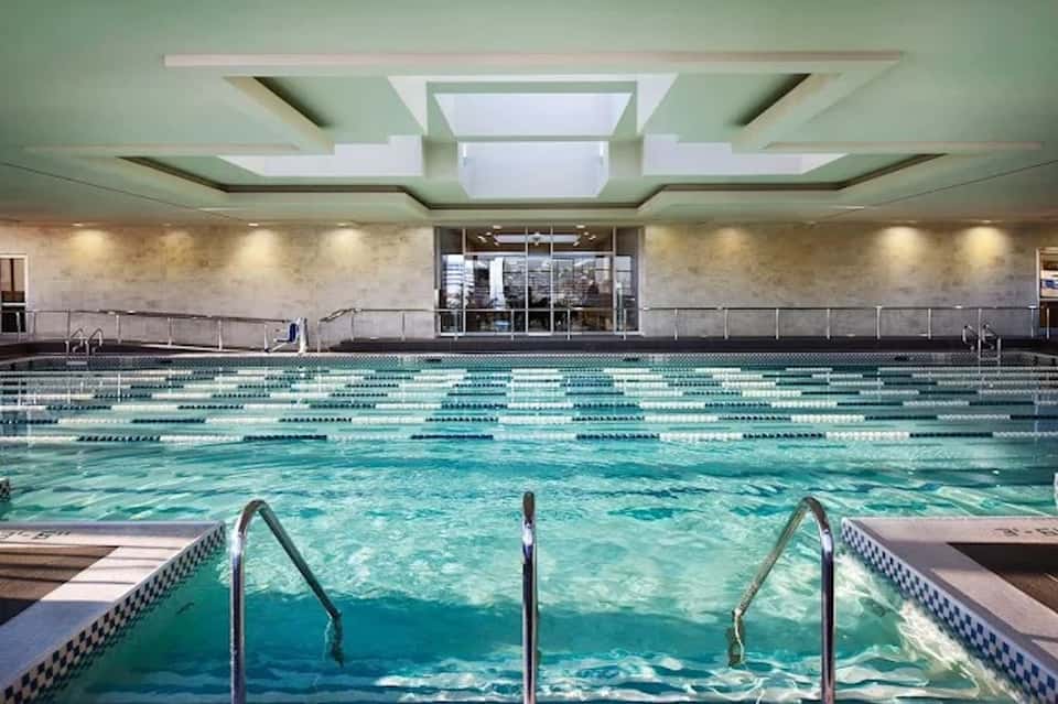 Indoor swimming pool with lane markers, skylight, green ceiling, and large windows in contemporary facility