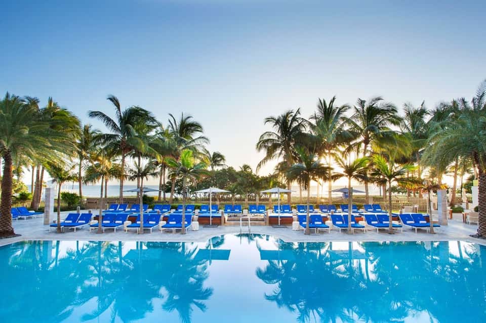 Luxury resort pool deck with blue lounge chairs, palm trees, and ocean view
