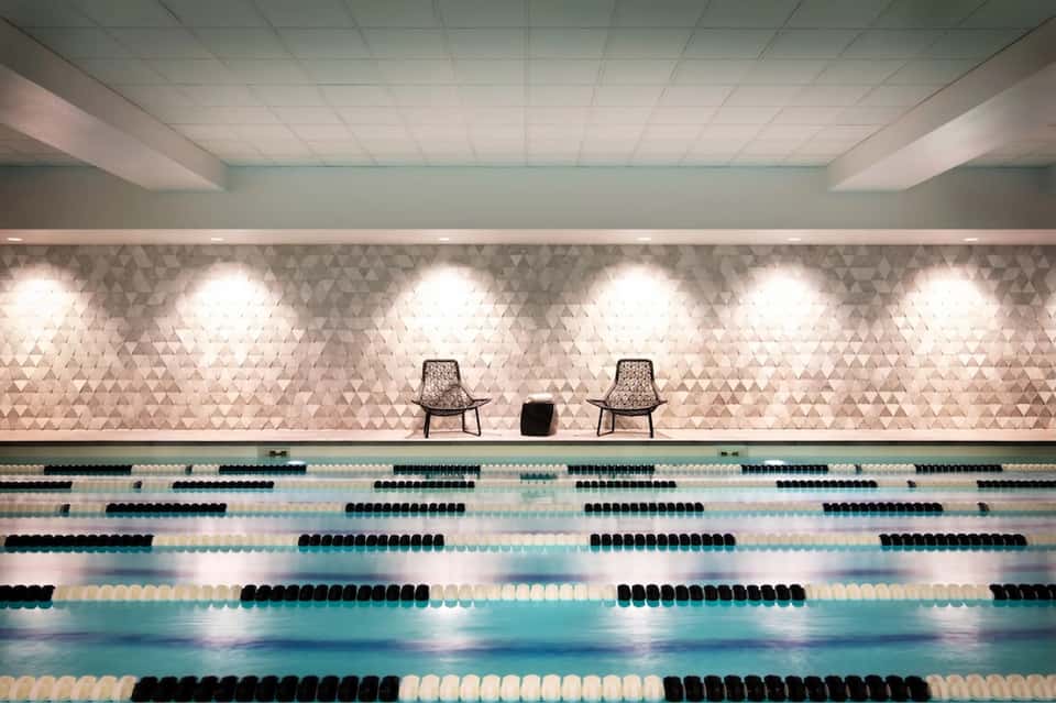 Indoor competition swimming pool with multiple lanes, geometric wall pattern, recessed lighting, and observation seating