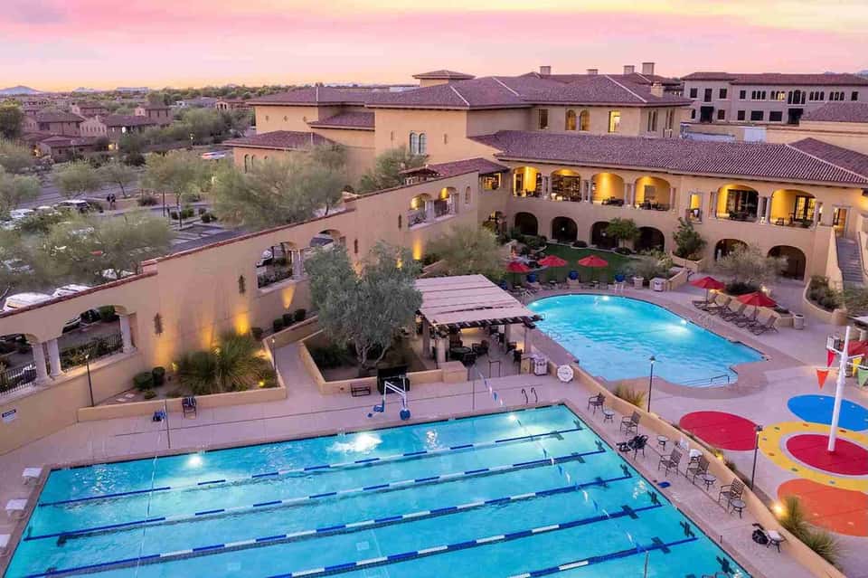Resort courtyard at sunset with lap pool, leisure pool, colonial architecture, red umbrellas, and mountain views