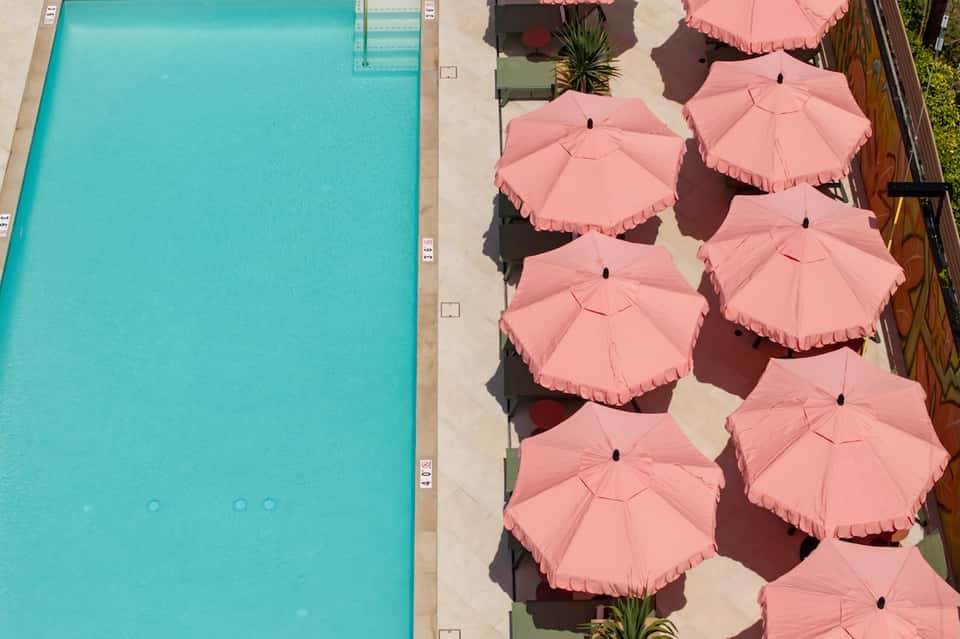 Aerial view of turquoise pool with pink fringe umbrellas lining the sundeck