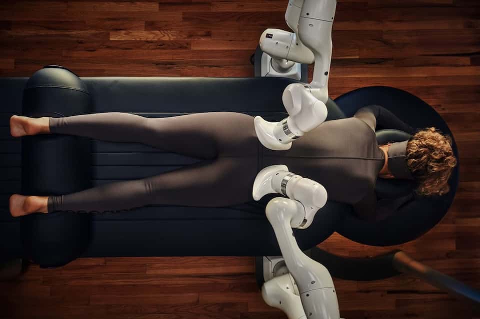 Person using white robotic exoskeleton leg apparatus on black leather couch