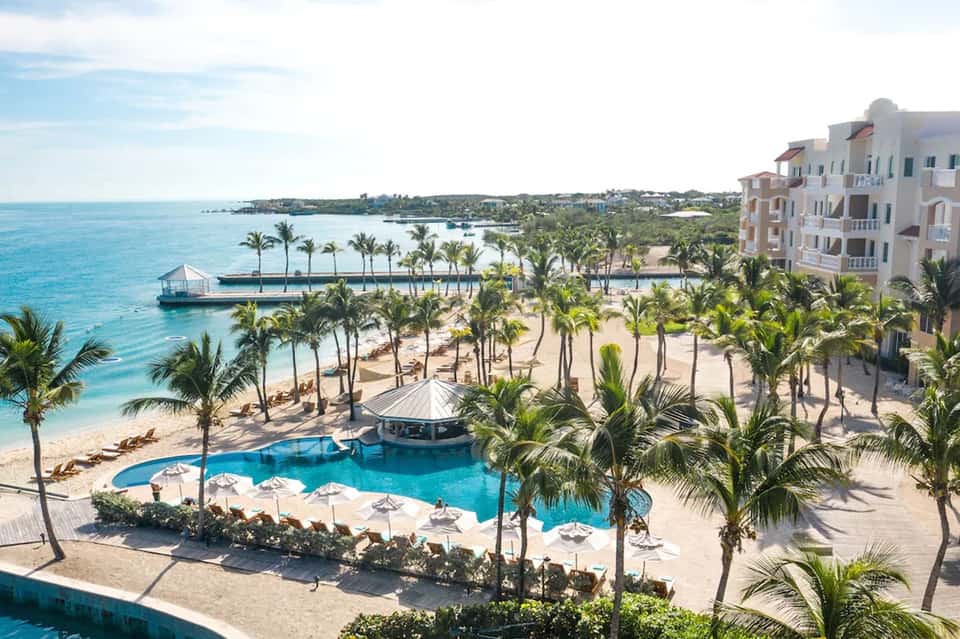 Beachfront resort aerial view with curved pool, palm trees, sandy beach, and turquoise ocean