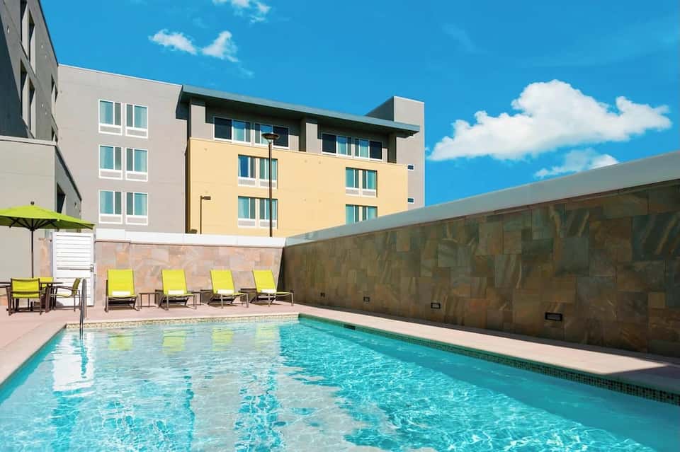 Urban hotel pool with bright yellow loungers, colorful building facade, and blue sky