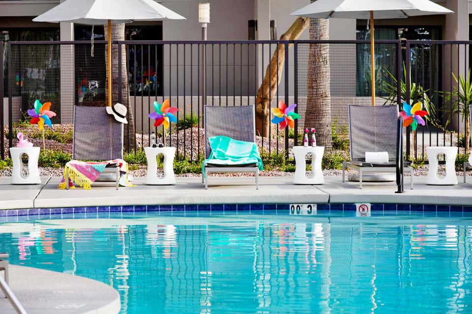 Colorful pool decorations including pinwheel toys and turquoise lounger by resort pool with fencing