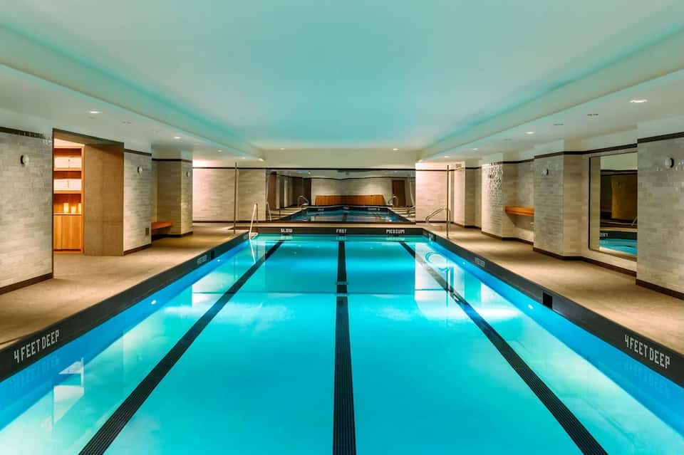 Indoor lap pool with turquoise water, lane dividers, illuminated ceiling, and modern spa facility architecture