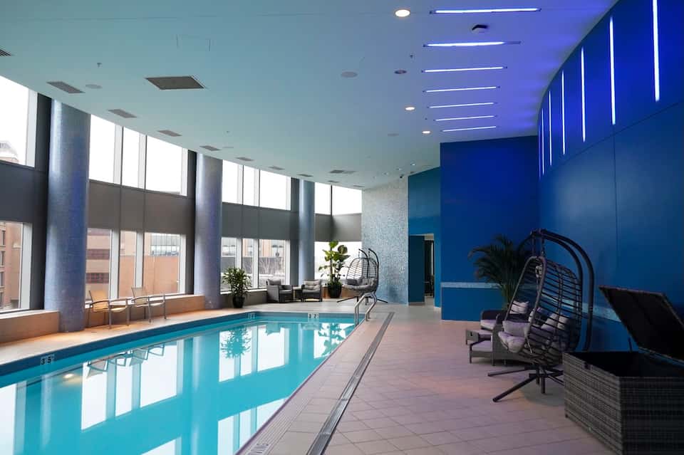Modern indoor pool with natural lighting, blue accent wall, and contemporary lounge seating