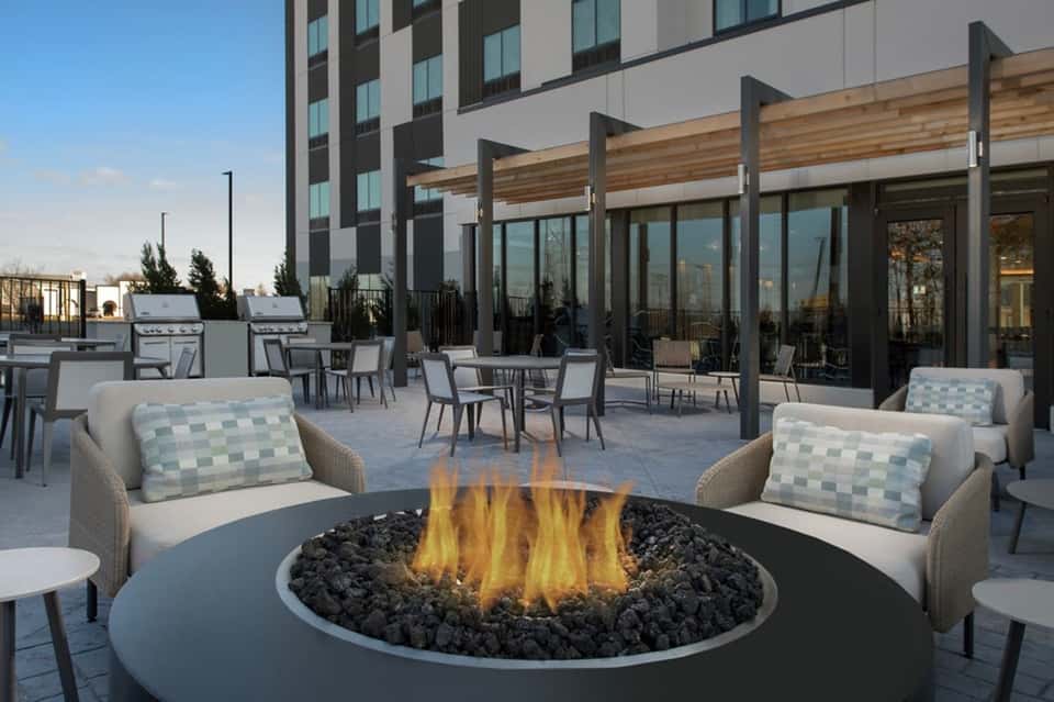 Rooftop terrace with fire pit, lounge seating, grills, and modern building with city views