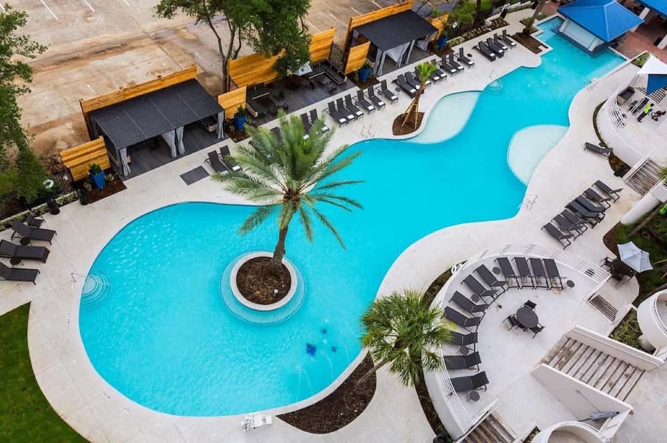 Aerial view of resort pool with curved shape, loungers, and tropical landscaping