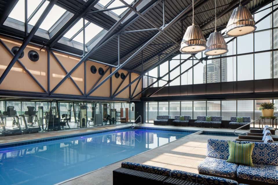 Indoor swimming pool with glass ceiling, industrial architecture, and city skyline views