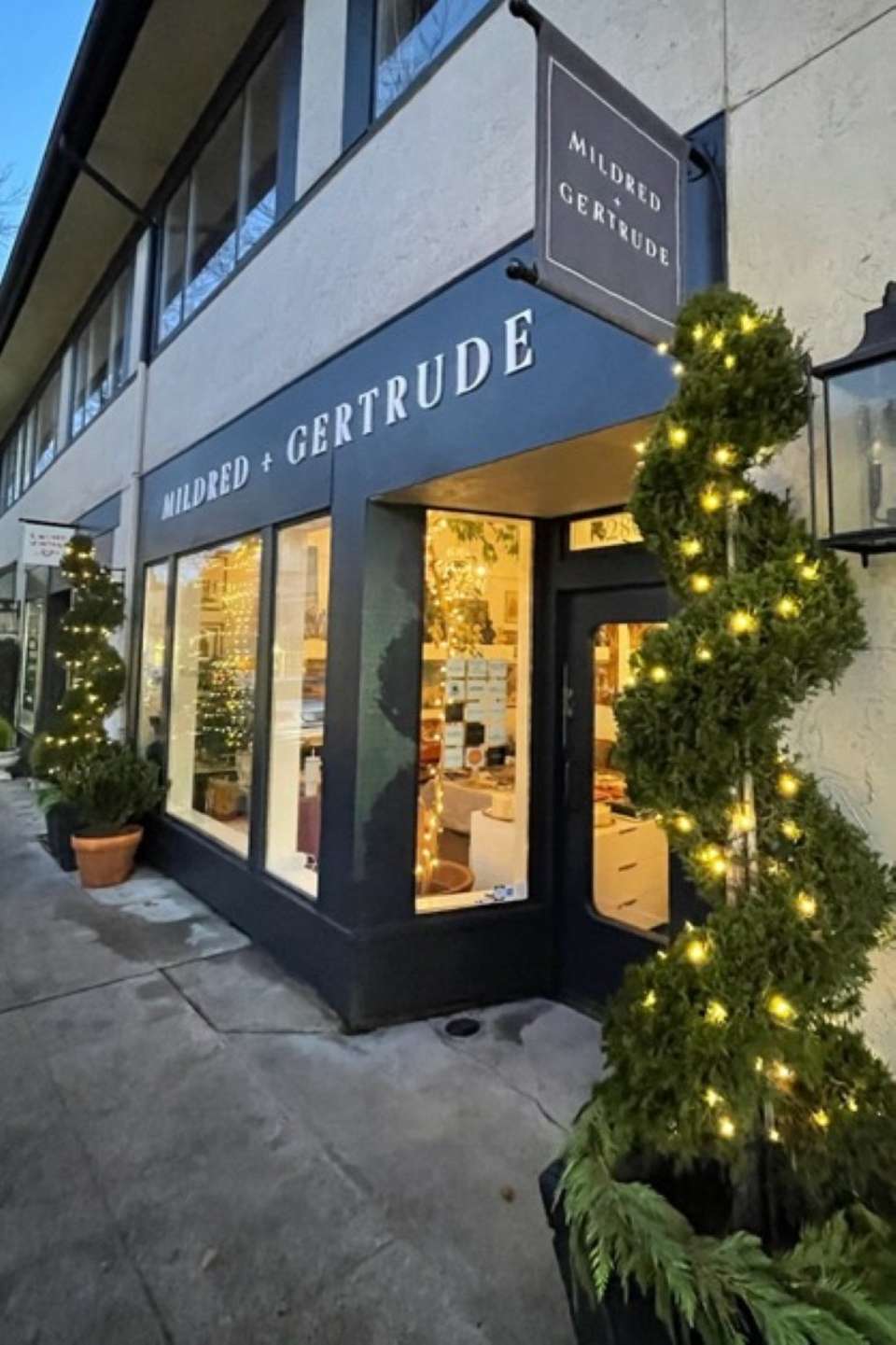 Mildred + Gertrude boutique storefront with holiday garland and illuminated window displays