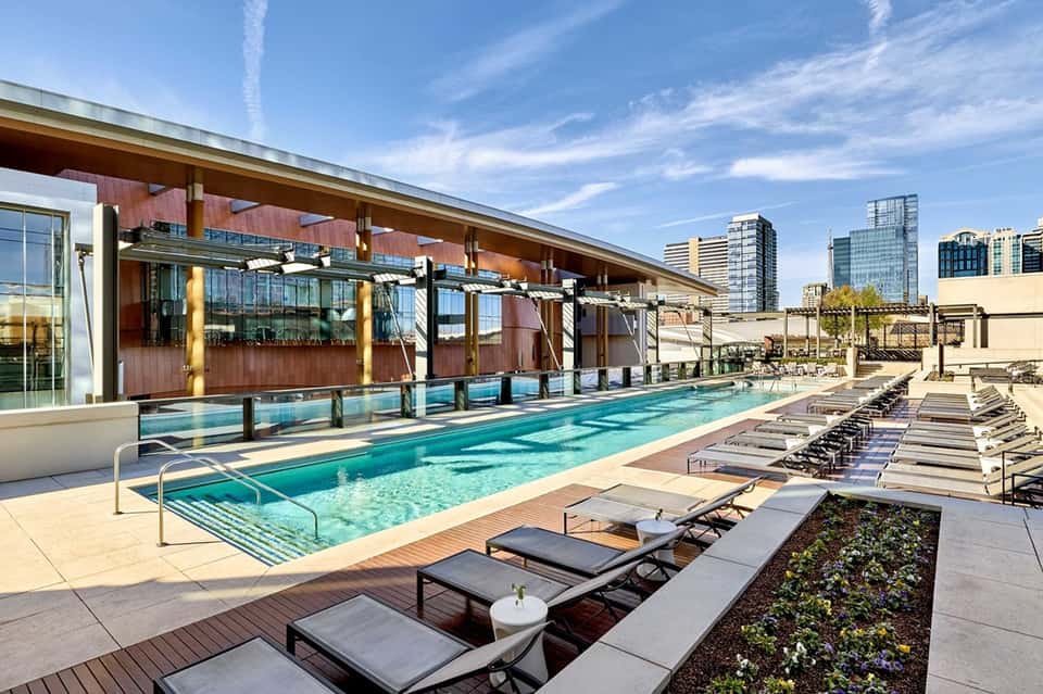 Modern rooftop pool with glass enclosure, city skyline views, and lounge seating