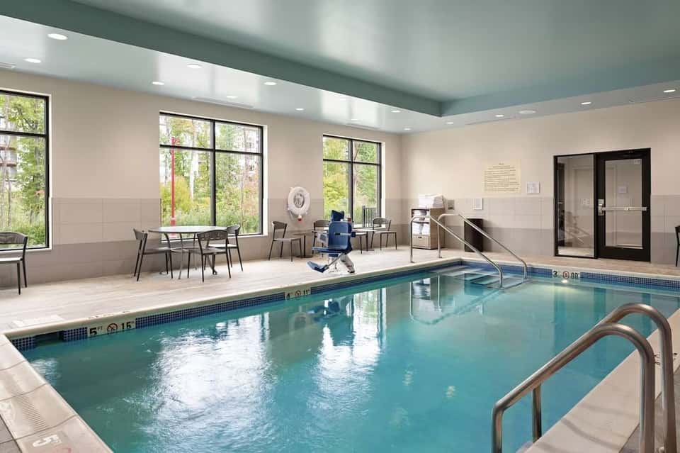Indoor swimming pool with bright windows, seating area, and modern architecture with teal ceiling
