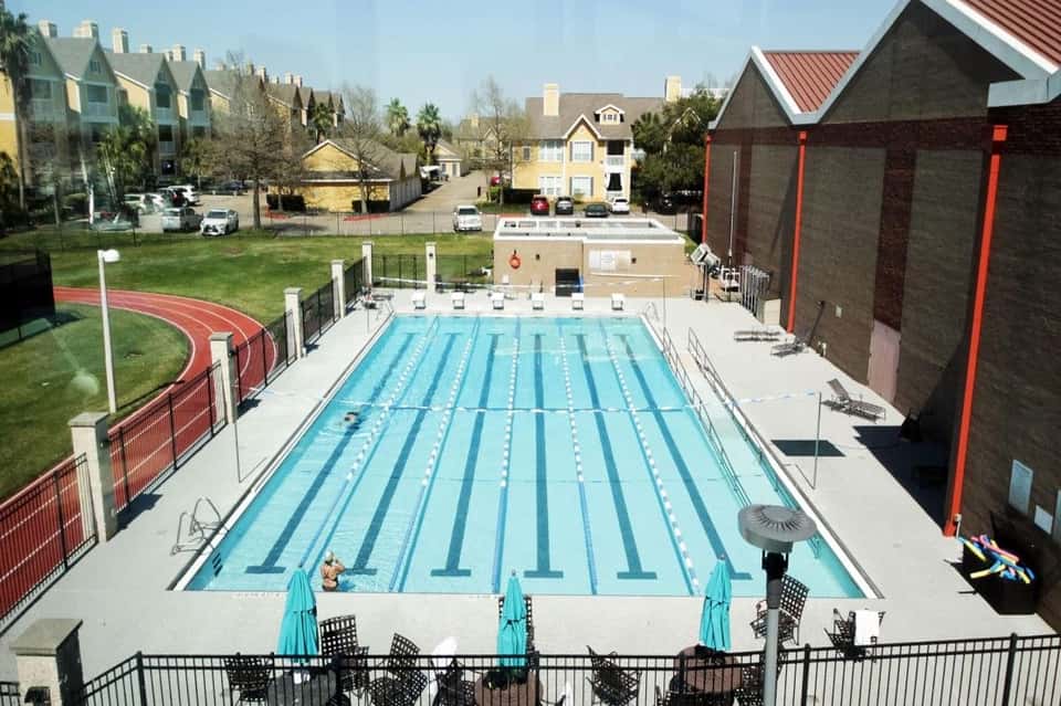 Olympic-sized indoor lap pool with lane dividers, seating area, and residential buildings in background