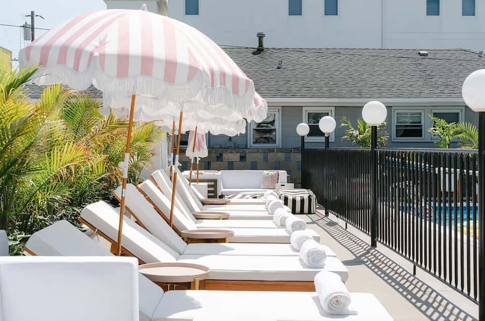 Beachfront hotel deck with striped pink umbrella, white loungers, and ocean view