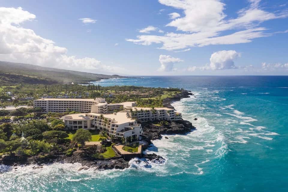 Aerial view of beachfront resort with white buildings on rocky coastline and turquoise ocean