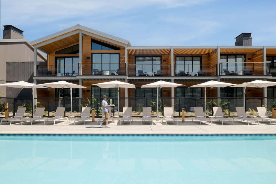 Modern resort building with wood accents, white umbrellas, lounge chairs, and pool in foreground