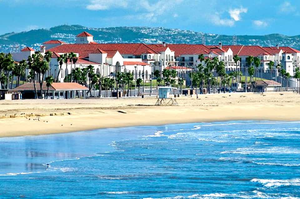 Beachfront resort with red-roofed buildings, palm trees, and sandy beach with ocean waves
