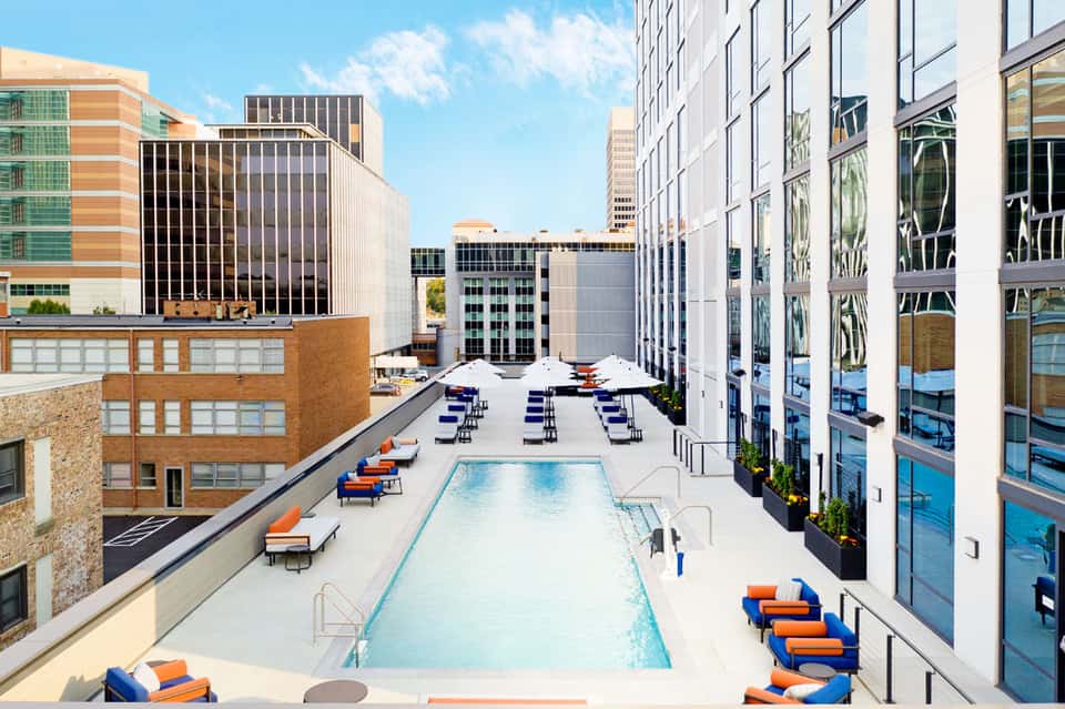 Rooftop pool deck with blue loungers, umbrellas, and modern high-rise buildings surrounding an urban resort