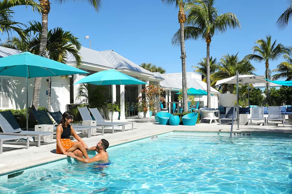 Family enjoying turquoise pool at tropical resort with white cabanas and palm trees under blue sky
