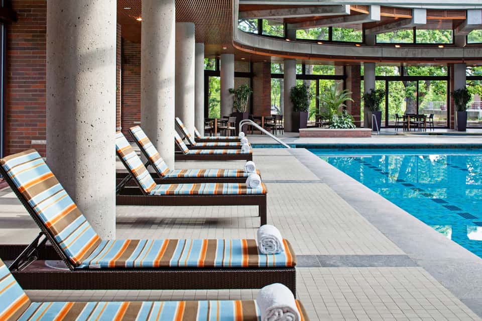 Indoor pool facility with striped lounge chairs, concrete columns, large windows, and brick architecture