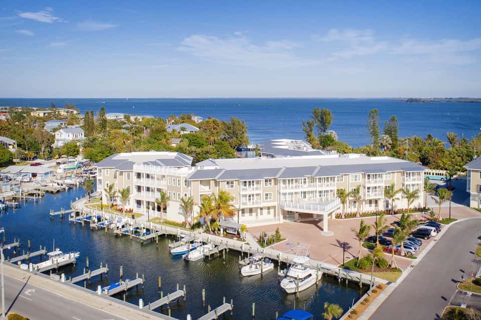 Waterfront resort with white multi-story buildings, boat docks, and blue water views under clear sky