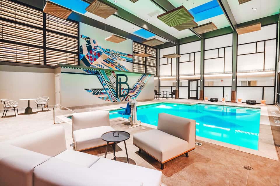 Modern indoor swimming pool with geometric art wall, white loungers, and skylights