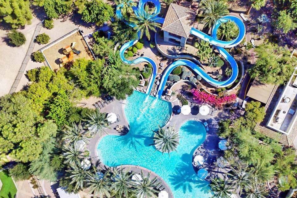 Aerial view of resort with turquoise pools, water slides, palm trees, and surrounding landscaping