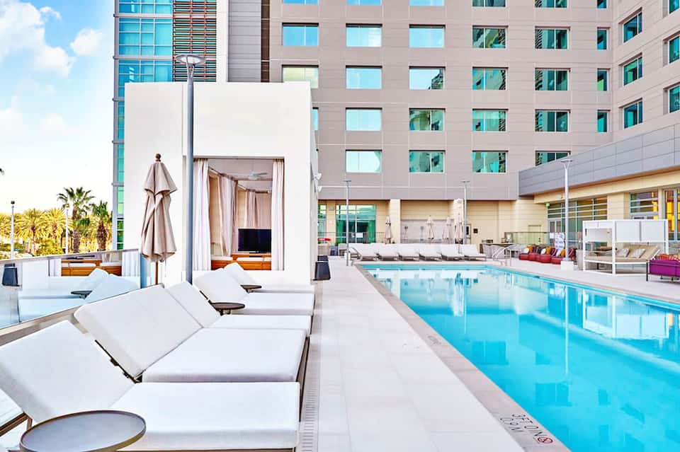 Modern hotel outdoor pool with lounge chairs, umbrellas, and multi-story building