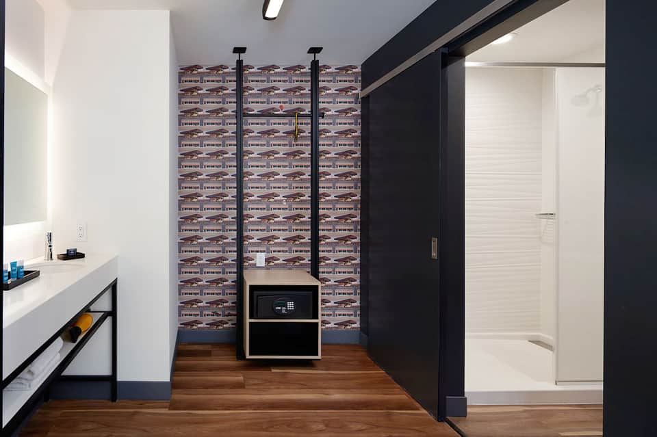 Modern bathroom with double vanity, shower enclosure, patterned accent wall, and microwave