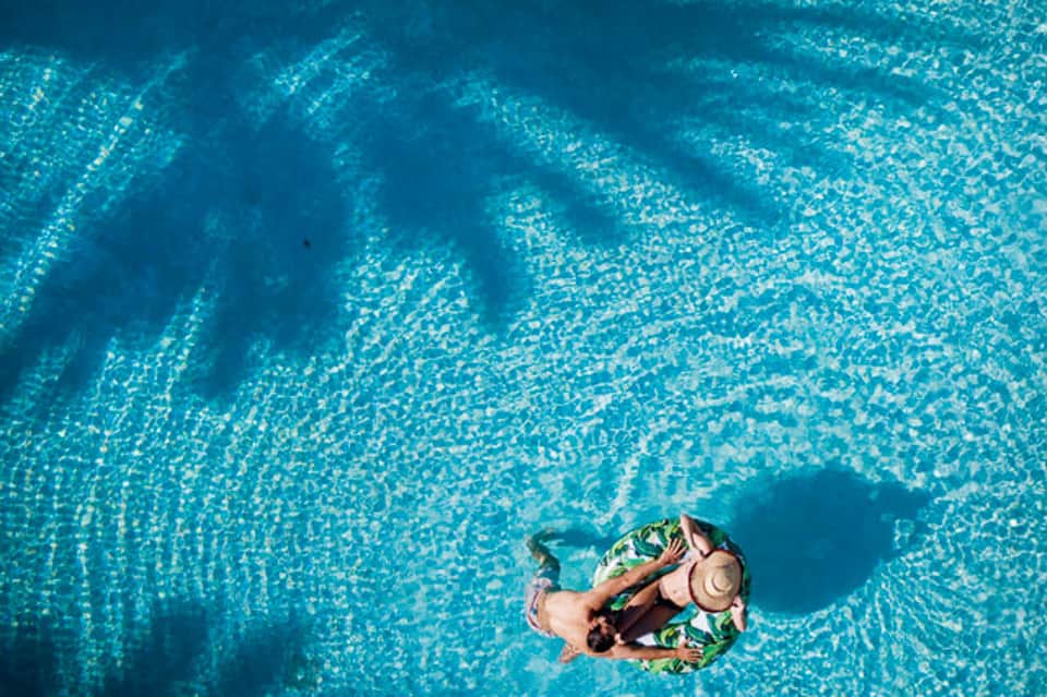 Aerial view of person floating on colorful raft in crystal clear turquoise pool water