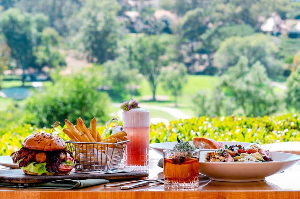 Gourmet burger and fries meal on table overlooking mountain valley and wildflower meadow