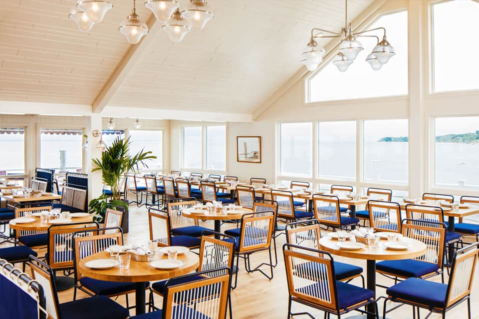 Bright dining room with wooden chairs, blue cushions, pendant lights, and expansive water views