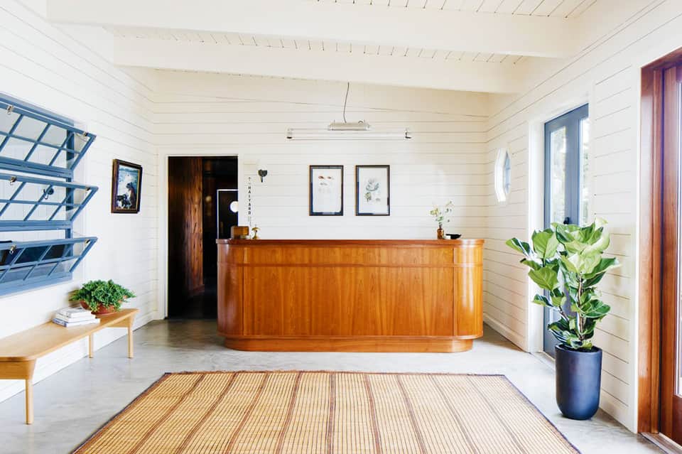 Modern hotel lobby with curved wooden reception desk, white shiplap walls, and blue shelving