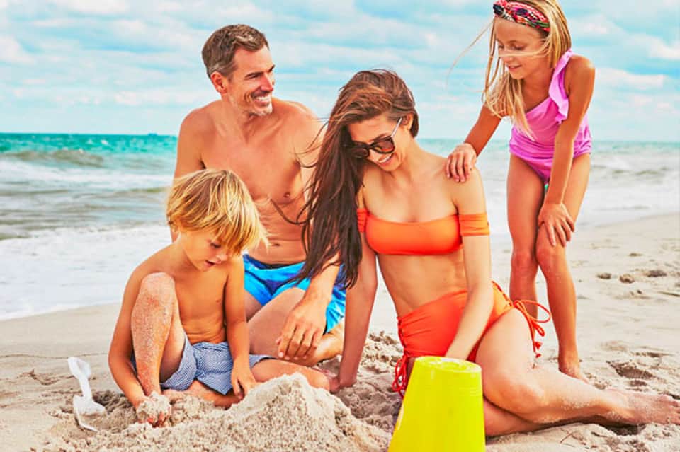 Family building sandcastle on beach with turquoise ocean and clear sky
