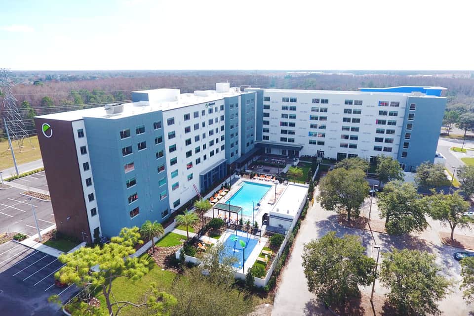 Aerial view of modern blue and white apartment complex with central pool and courtyard surrounded by landscaping