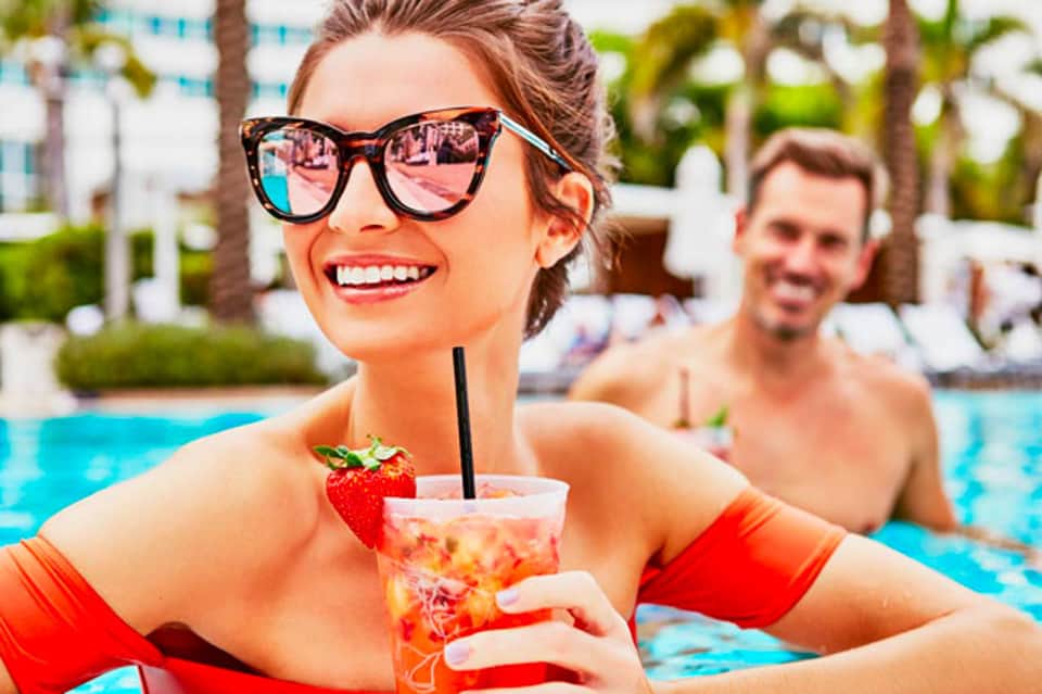 Woman in red swimsuit enjoying tropical cocktail by resort pool with palm trees