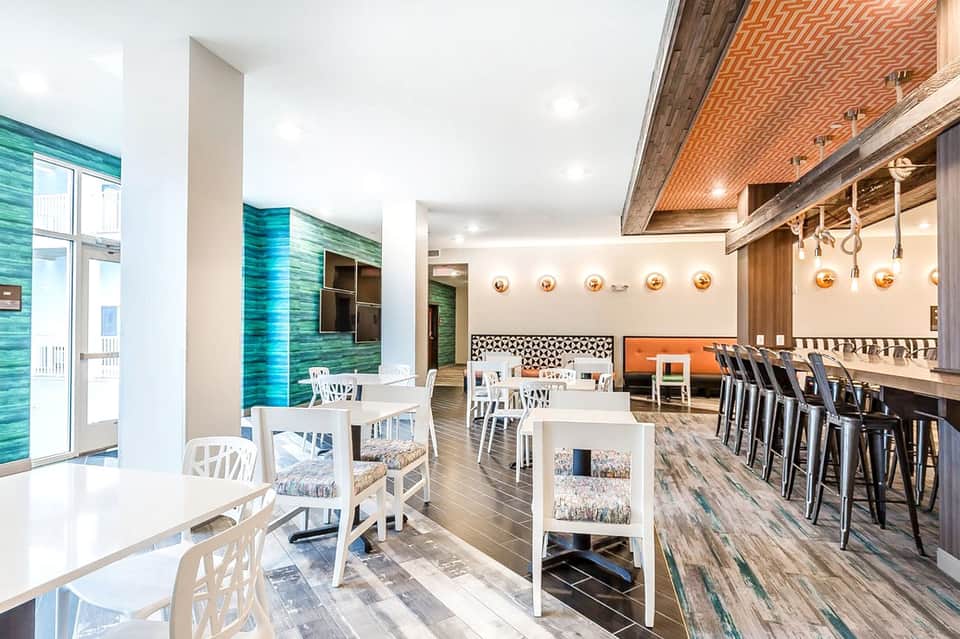 Modern resort dining area with turquoise accent walls, white chairs, and copper pendant lighting