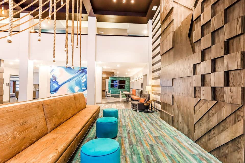 Modern hotel lobby with wooden beams, rope pendant lights, colorful artwork, and blue seating