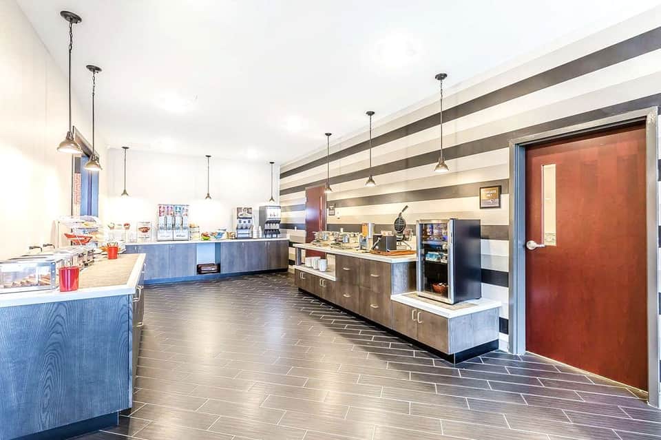 Modern hotel café with blue wood cabinetry, pendant lights, striped ceiling, and display cases with refreshments