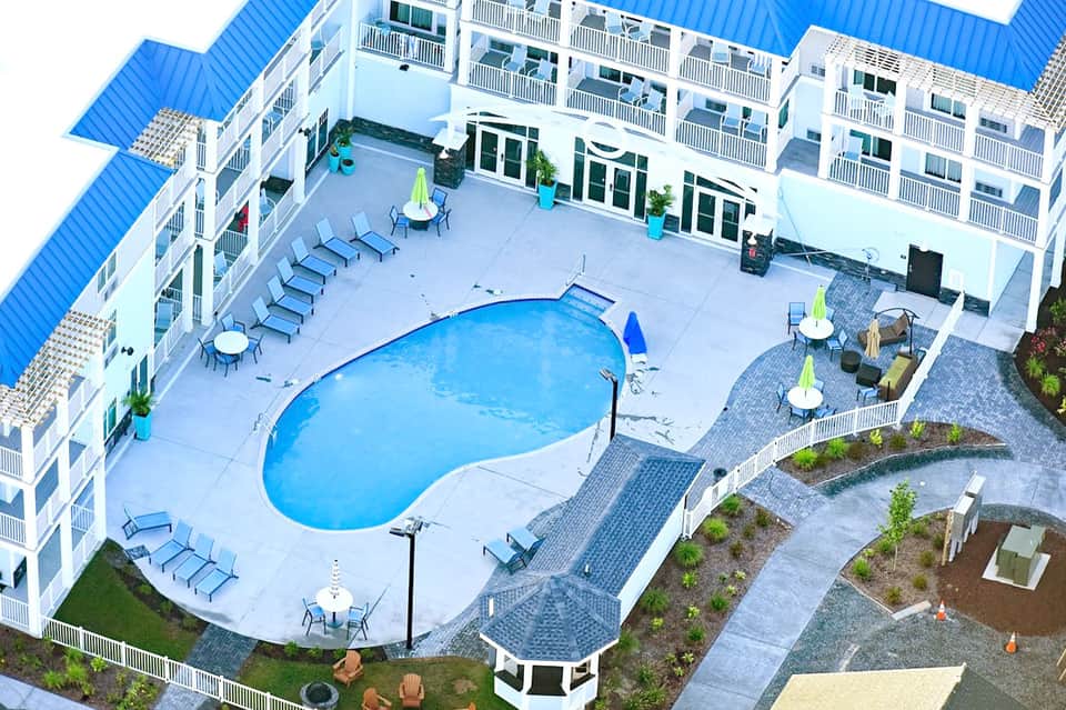 Aerial view of resort with kidney-shaped pool, lounge chairs, and white multi-story building