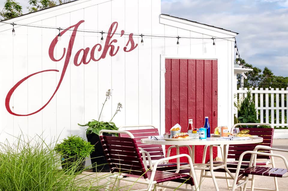 Outdoor dining patio at Jack's restaurant with red and white chairs, striped umbrellas, and white building facade