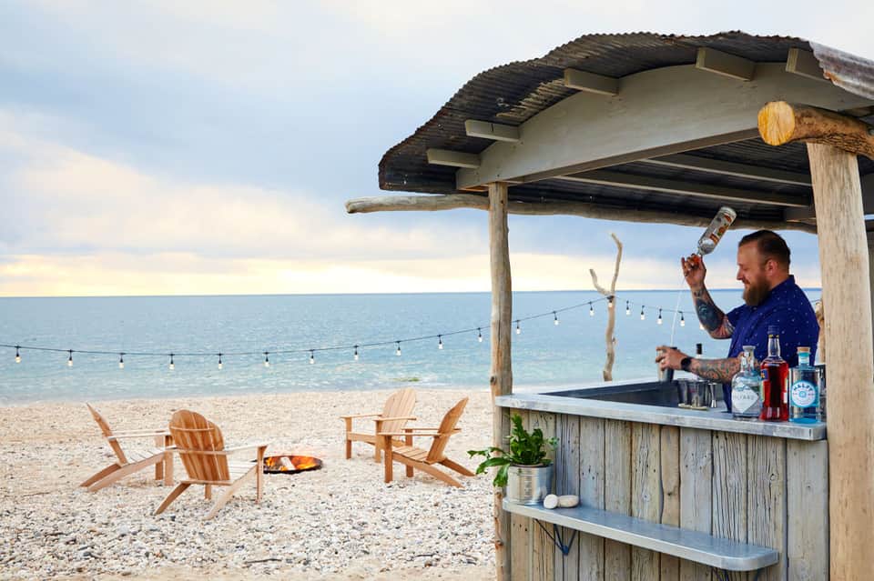 Beachfront bar with wooden pergola, Adirondack chairs, and ocean view at dusk