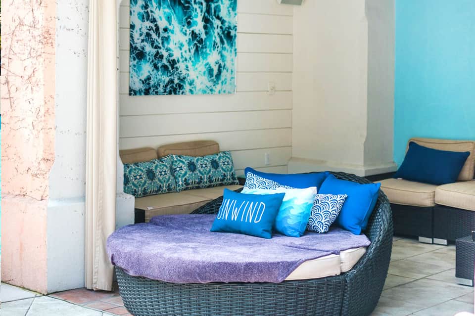 Woven daybed with purple mattress and blue patterned pillows in a coastal setting